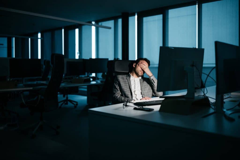 A smartly-dressed businessman is resting in his office in front of his computer. He is tired and wants to go home.