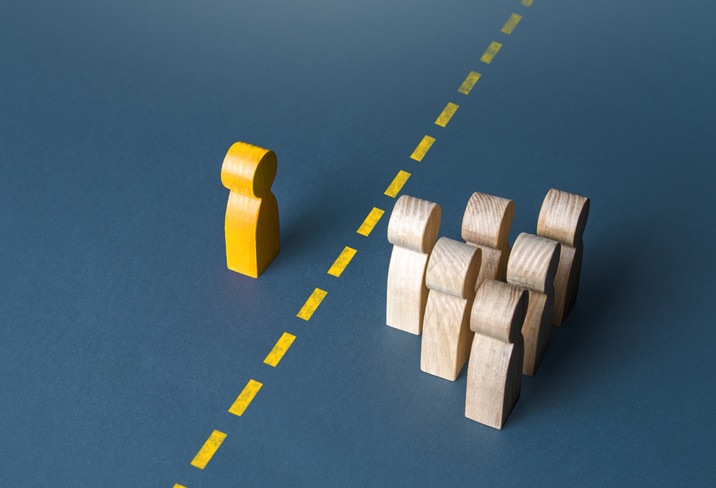 A yellow wooden figure is separated from a group of plain, wooden figures by a dashed, yellow line, symbolizing boundary setting,