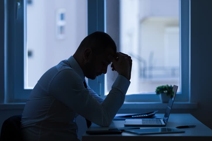 A silhouette of a man hunched over his desk, thinking of leadership identity coaching.