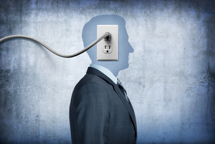 An electrical cord is plugged into a electrical outlet that sits on the face of an unrecognizable businessman.