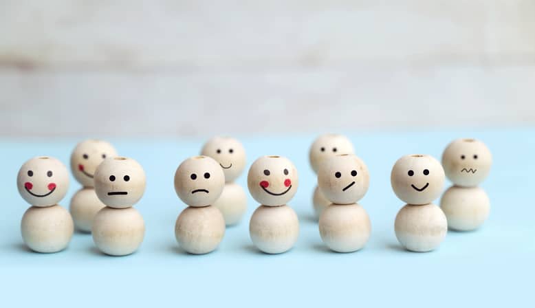 Rows of wooden figures with different emotions drawn on their faces symbolizing emotional intelligence coaching.
