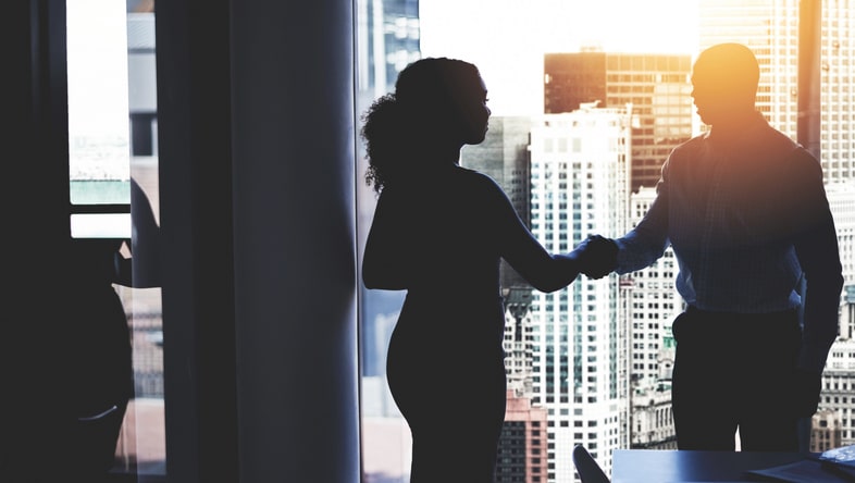 A woman shakes the hand of an executive coach, offering executive coaching services, in front of a city skyline.
